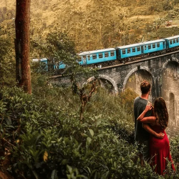 Blue train traveling over the Nine Arches Bridge surrounded by green hills in Ella, Sri Lanka.