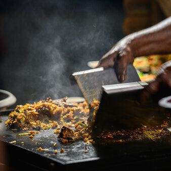 Sri Lankan street food vendor cooking spicy kottu roti on a hot griddle.